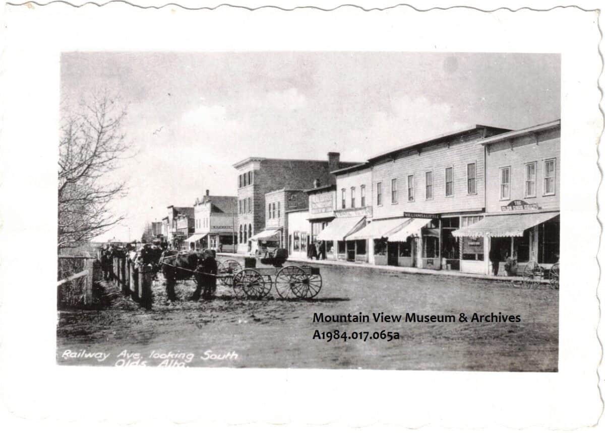 Railway Avenue, Olds, Alberta, ca 1910, showing horses with buggies hitched, across the street from stores.