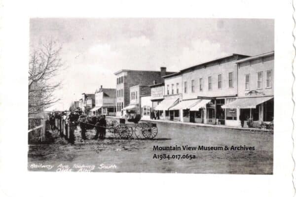 Railway Avenue, Olds, Alberta, ca 1910, showing horses with buggies hitched, across the street from stores.