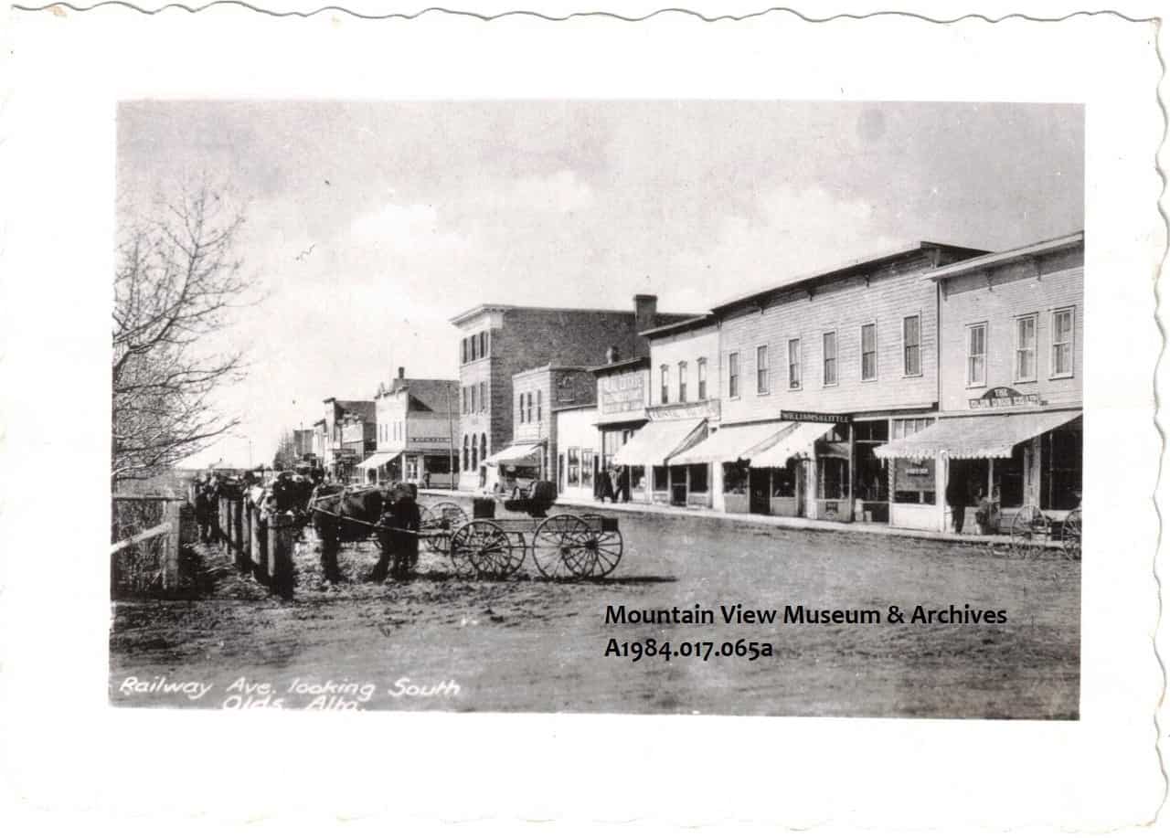 Railway Avenue, Olds, Alberta, ca 1910, showing horses with buggies hitched, across the street from stores.