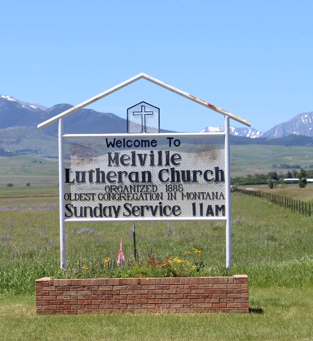 White wrought-iron marker in front of the white-painted Melville Lutheran Church, Montana, built in 1914.