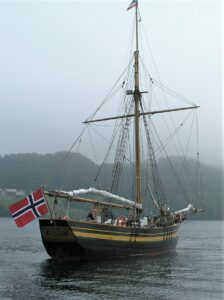 The replica of the emigrant sloop "Restauration" in the island of Sjernarøy's protected Ramsvig cove, 2013. The Norwegian flag is flying in the wind.